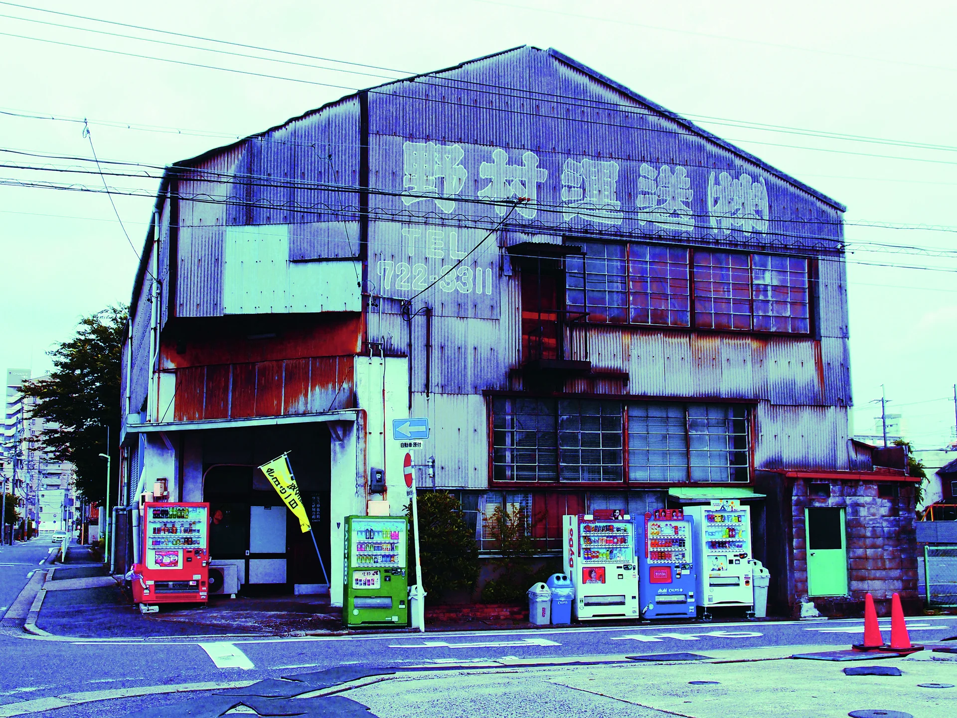 Vending machines line a heavily weathered industrial corner building with broad faded upper lettering.