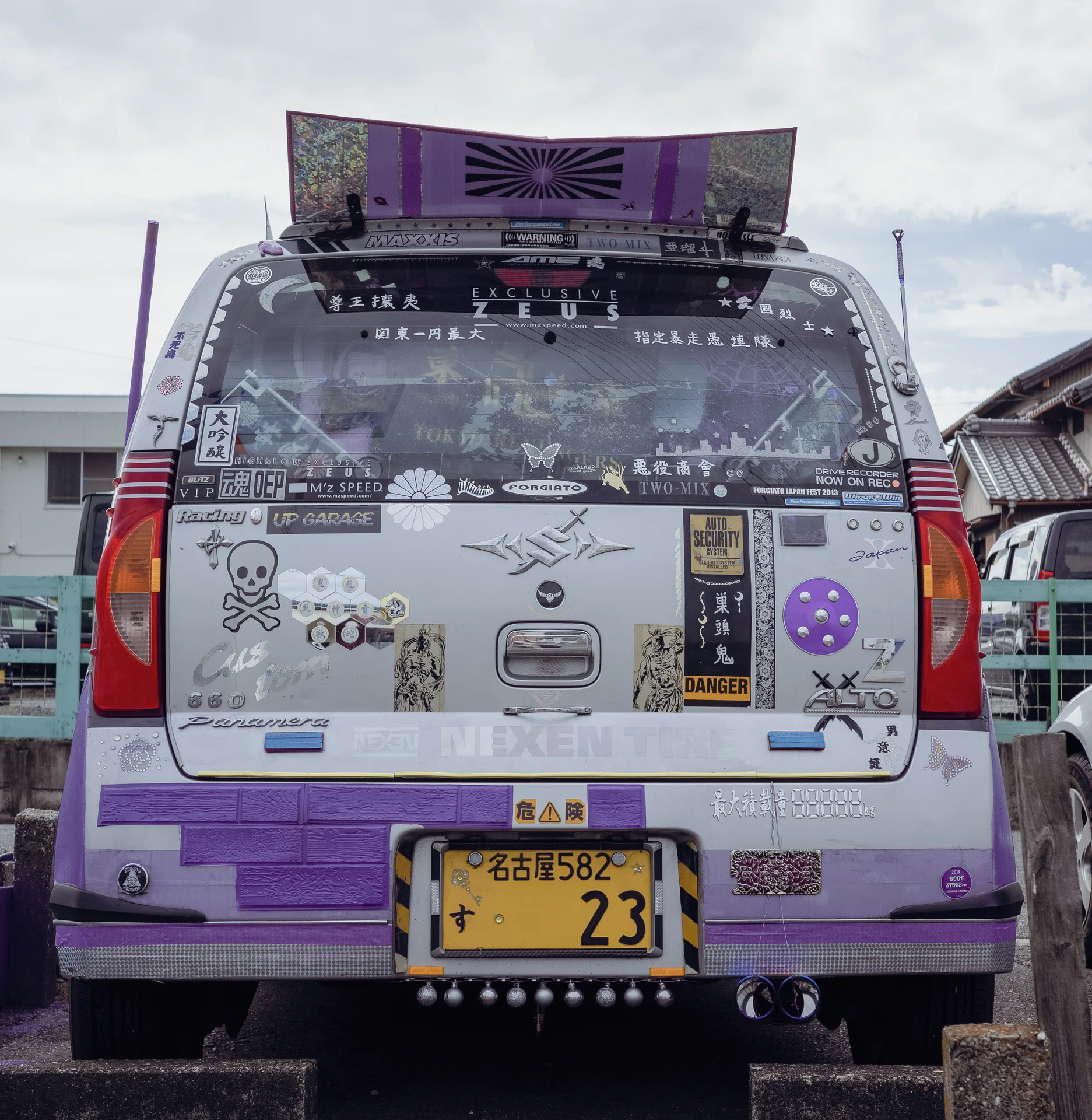 The rear of a small pale vehicle is densely decorated with stickers, purple trim and a rooftop panel.