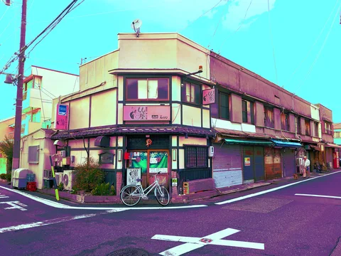 A long corner building with closed storefront shutters faces a bicycle and painted road markings.