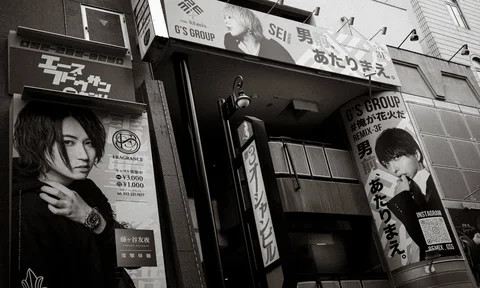 Large portrait advertisements surround a recessed building entrance beneath projecting signs in black and white.