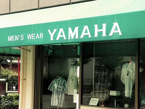 White MEN'S WEAR YAMAHA lettering spans a green fascia above windows displaying pale shirts.