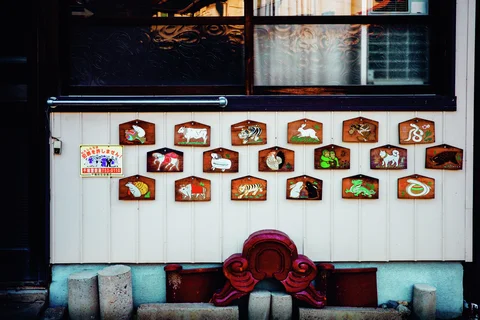Painted animal plaques hang in three rows beneath a patterned window on a white wall.