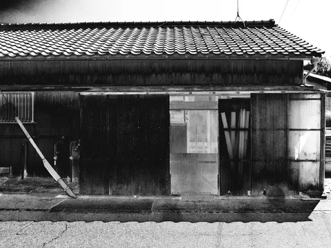 A broad tiled roof shades a patched wooden facade with a narrow doorway in black and white.