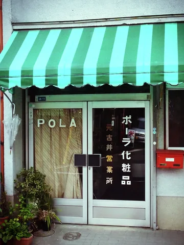 A green-and-white striped awning shelters a curtained glass shop entrance with a red wall-mounted mailbox.