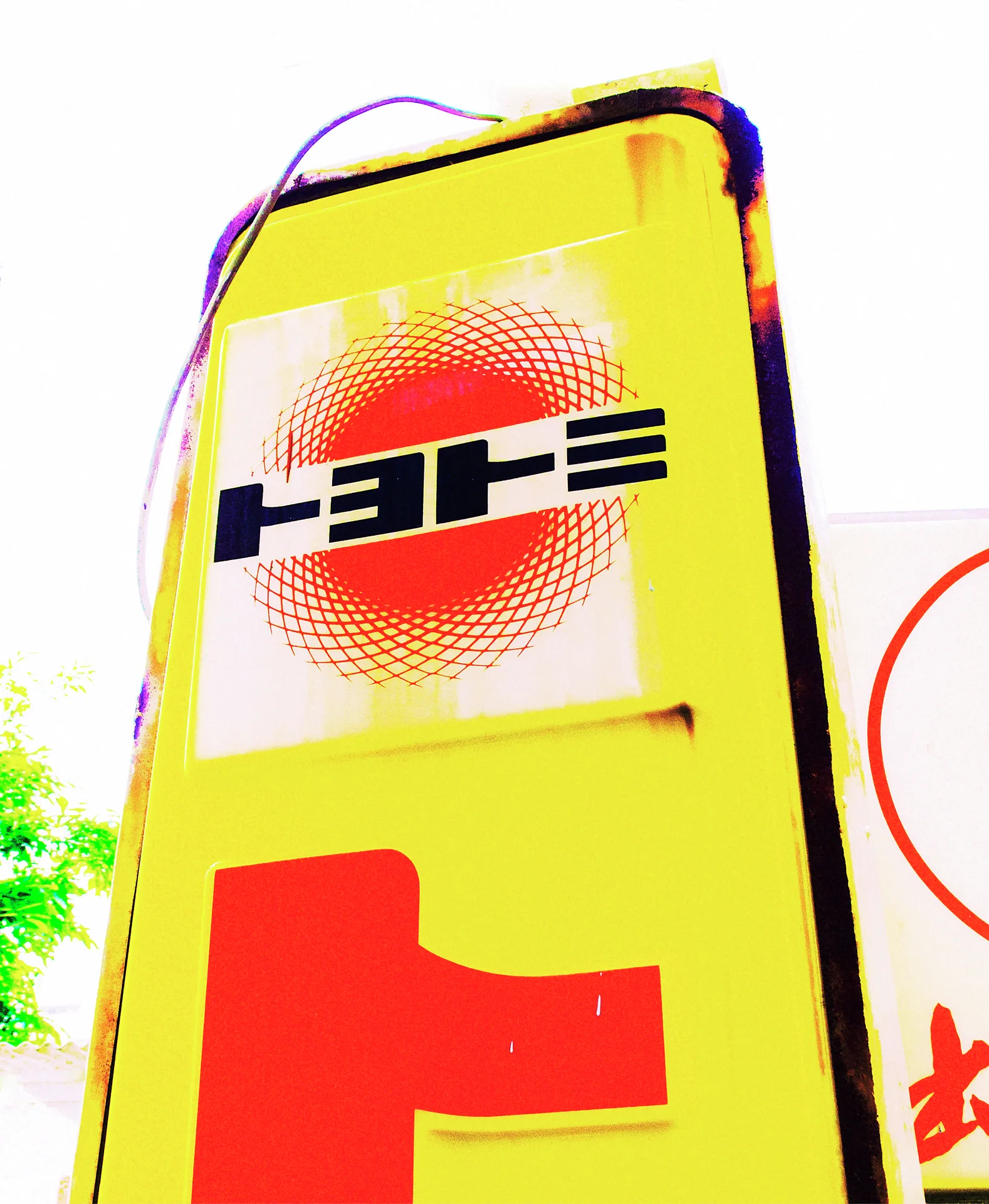 A tall yellow sign has dark lettering across a red dotted circle above a large red character.