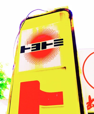 A tall yellow sign has dark lettering across a red dotted circle above a large red character.