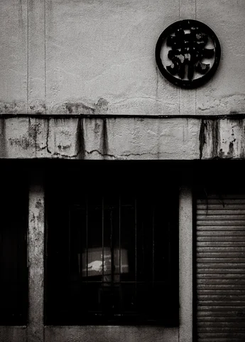 A circular wall emblem hangs above a dark recessed doorway and closed shutter in black and white.