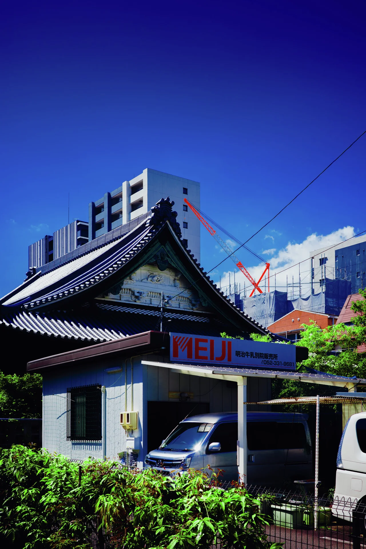 A curved tiled roof rises above a small carport with parked vehicles and surrounding greenery.