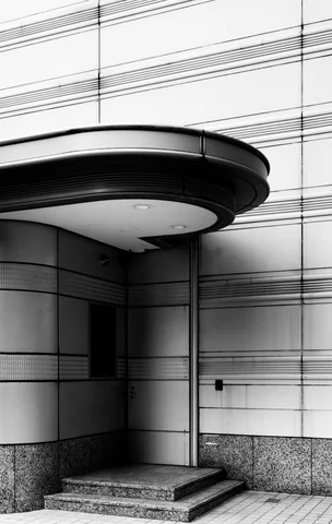 A rounded canopy shades a recessed entrance above three shallow steps within a horizontally patterned facade.