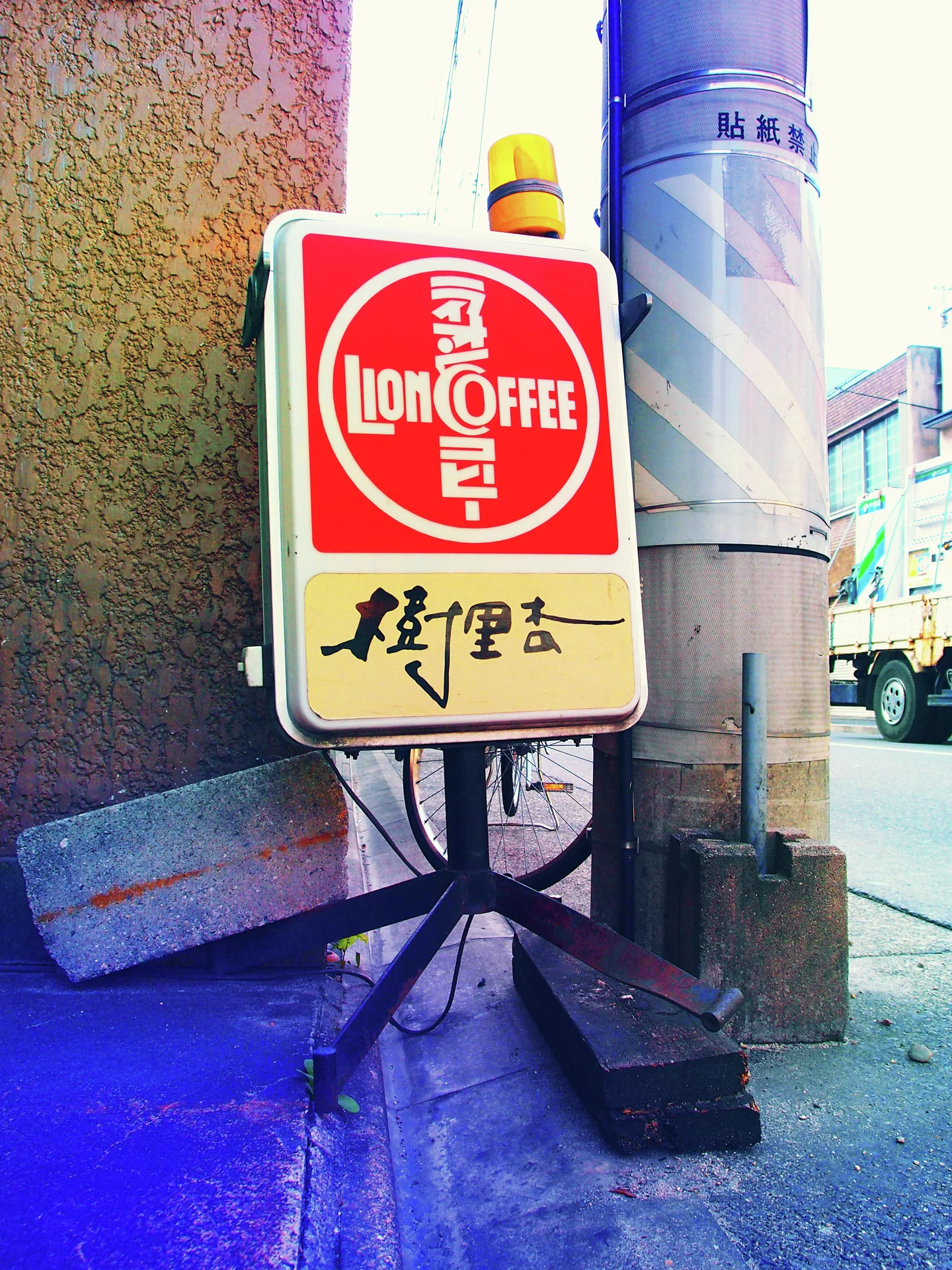 A red and cream coffee sign topped by a yellow light stands beside a striped utility pole.