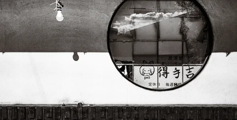 A round mirror reflects clouds and a sign above a white wall in black and white.