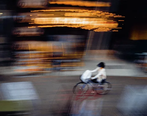 A cyclist passes a storefront smeared into horizontal orange light trails and dark streaks.