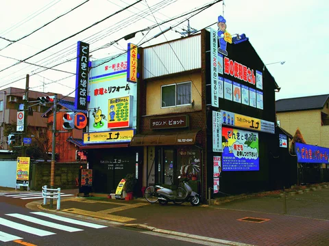 Colorful vertical signs crowd a corner building above a pedestrian crossing and parked scooters.
