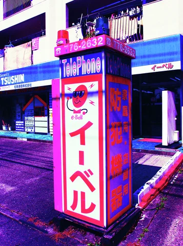 A pink and blue telephone-themed sign tower stands beside a shop-lined street.