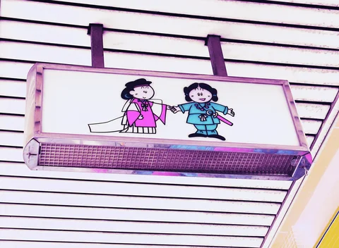 A projecting sign shows two cartoon figures in pink and blue against white horizontal siding.