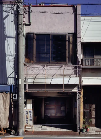 A narrow weathered building has dark upper windows and an empty awning frame above its entrance.