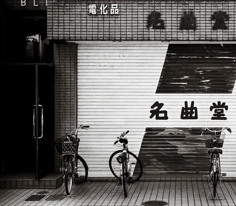Three bicycles stand before a striped metal shop shutter with bold lettering in black and white.