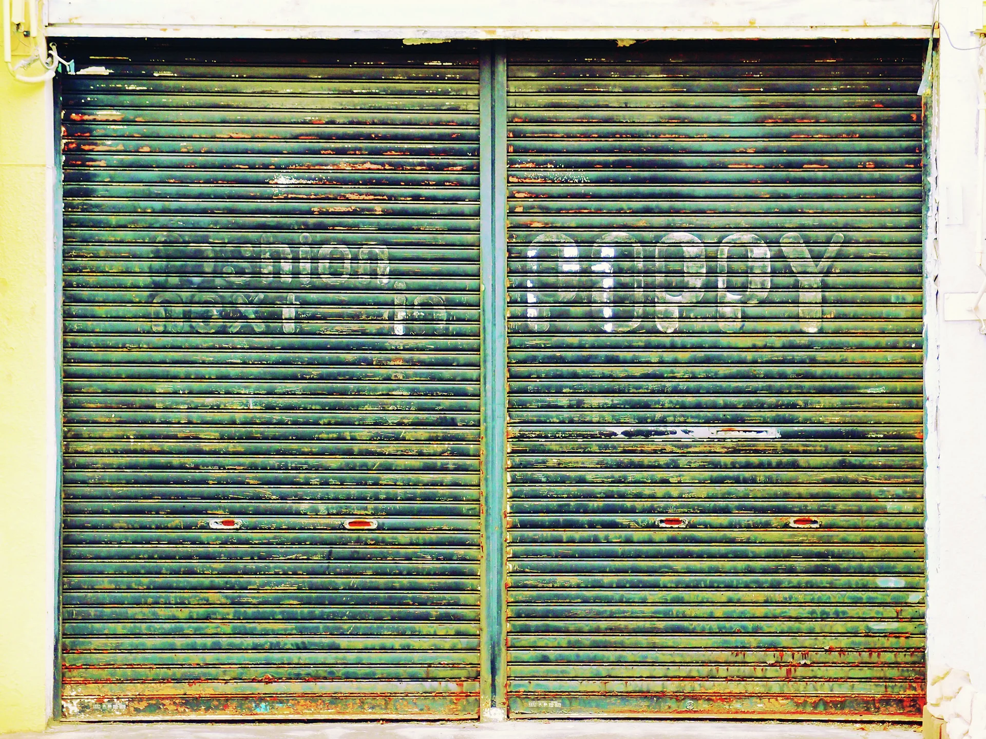 Faded white COPY lettering spans two rust-streaked green metal shutters in a pale frame.