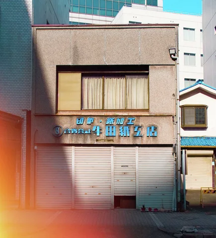 Blue raised lettering marks a small beige building above closed shutters and a curtained upper window.