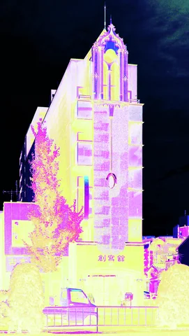 A tall pointed building appears in bright yellow and purple tones against a nearly black sky.