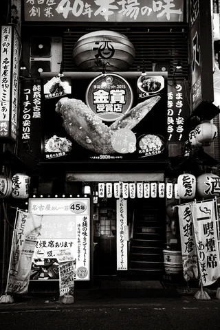 Lanterns and densely arranged illustrated signs surround a narrow restaurant entrance in a black and white view.