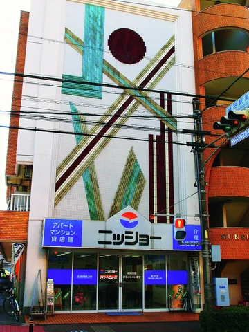 Crossing diagonal bands and a dark red circle decorate a tall narrow facade above a blue storefront.