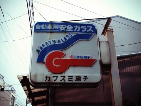 A weathered projecting sign displays blue SAFETY GLASS lettering and a large red-and-blue emblem beneath wires.
