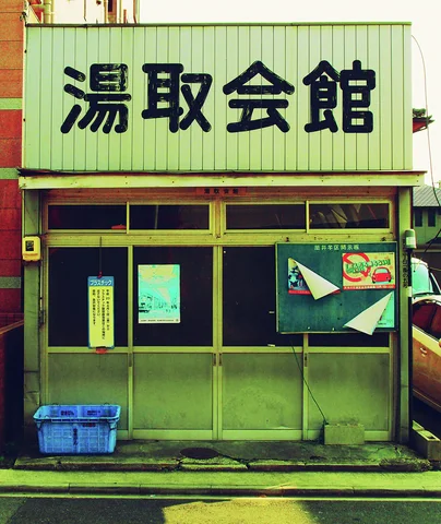 Large dark Japanese characters span a pale sign above sliding doors, notices, and a blue crate.