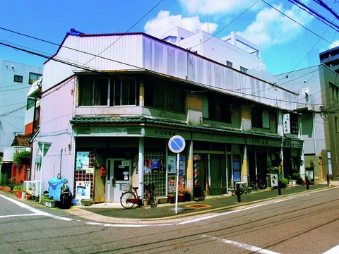 A weathered two-story corner building has long dark upper windows and several small ground-floor storefronts.