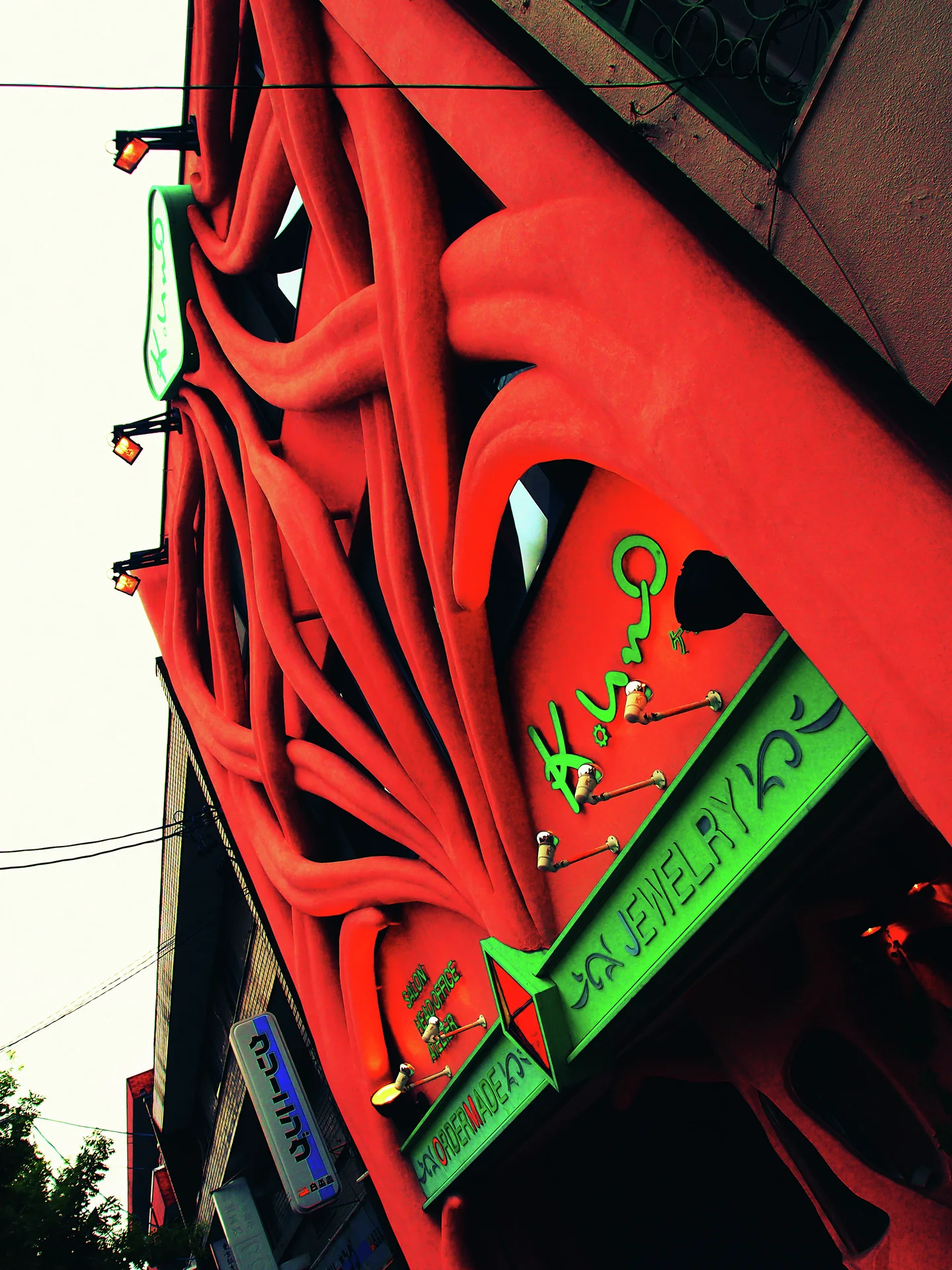 Large red branching decorative forms cover a storefront facade above small green signs.