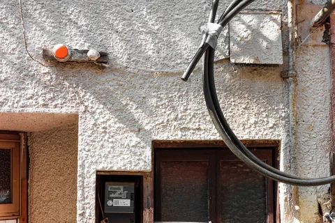 Black cables loop across a rough white wall above dark wooden doors and small utility fixtures.