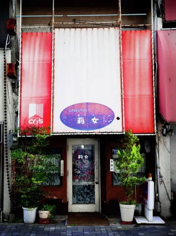 Red and white vertical panels frame a narrow shop entrance bordered by potted shrubs.