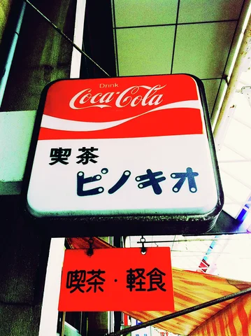 A red and white Coca-Cola sign projects above a smaller orange sign bearing black lettering.