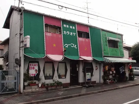 Alternating green and pink rounded panels decorate a two-story storefront with small windows and a striped awning.