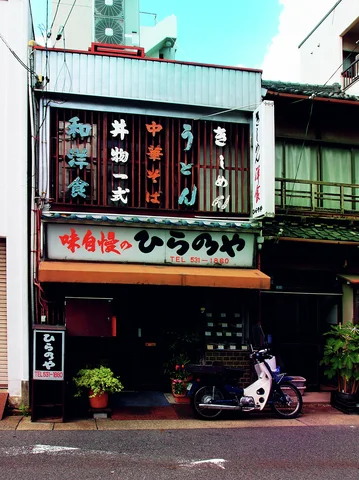 Japanese menu lettering covers upstairs windows above a dark storefront with potted plants and a parked scooter.