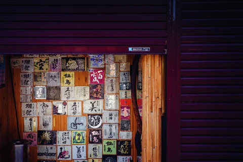A patchwork of illustrated labels covers a wooden door beneath a partly lowered shutter.