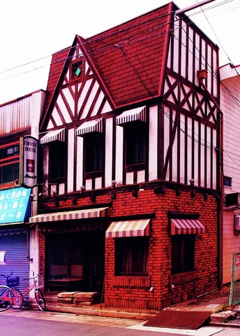A steep red gabled roof crowns a narrow building with decorative dark timber patterns and brick lower walls.