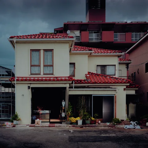 Red tiled roofs step across a cream building with potted flowers along its open ground-floor frontage.