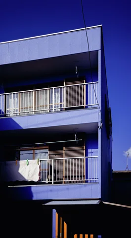 Metal balcony railings and a hanging white cloth punctuate a blue building facade beneath clear sky.