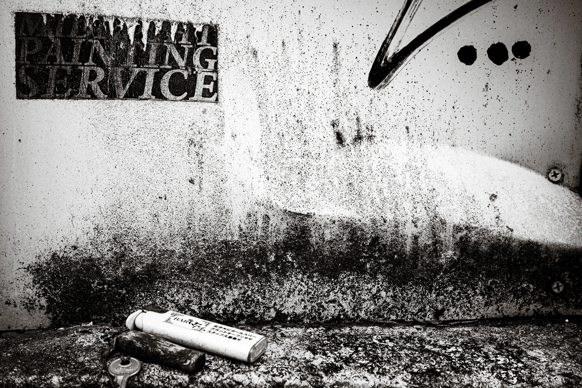A discarded can lies below a heavily stained wall bearing faded service lettering in black and white.