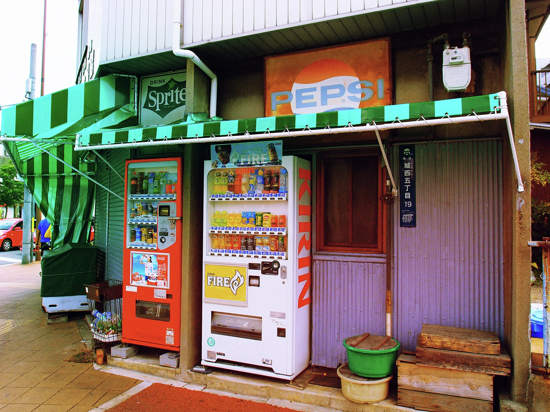 Red and white drinks vending machines stand beneath green-striped awnings and faded soft-drink signs.