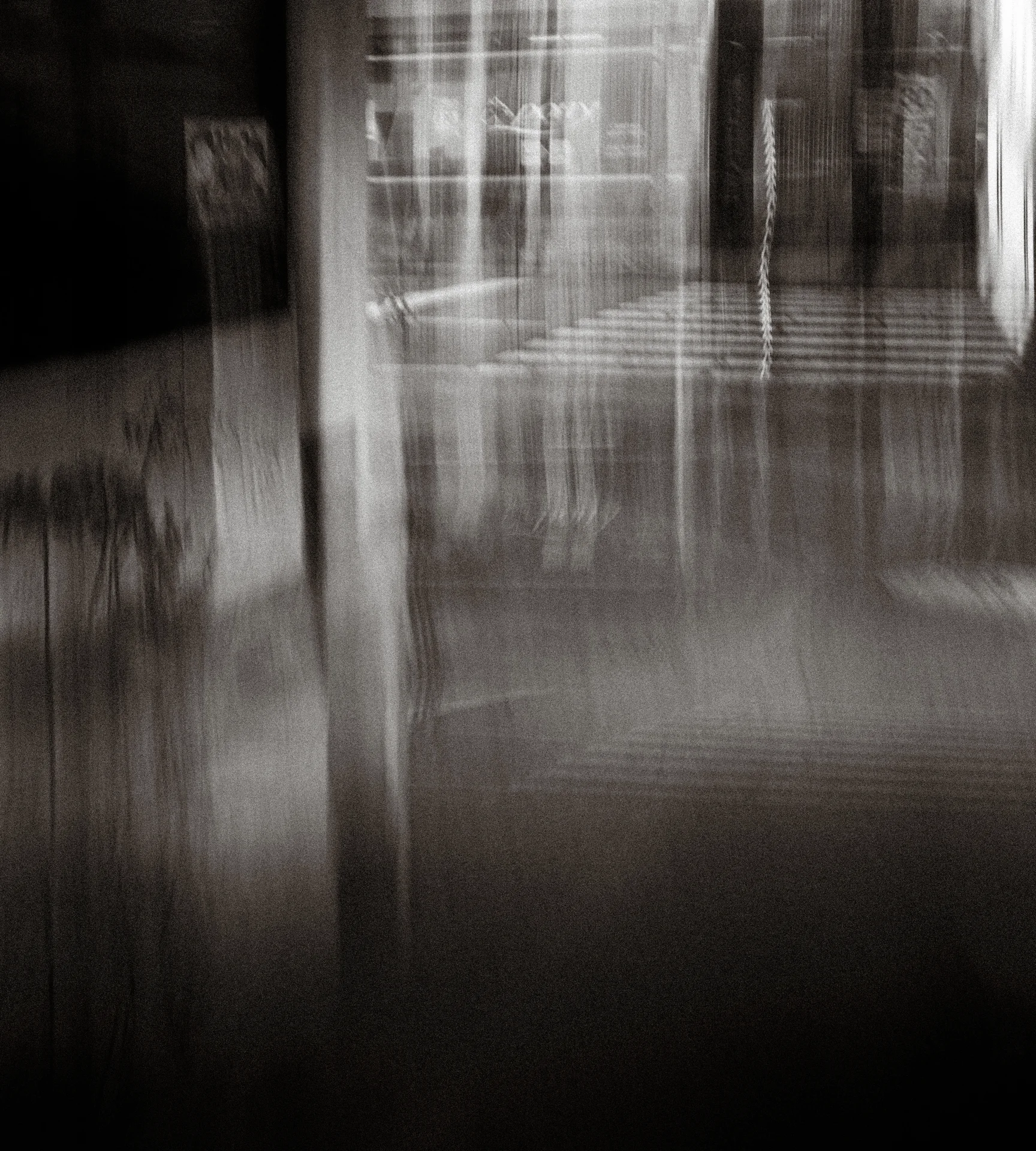 Vertical architectural lines dissolve into pale streaks above deep shadow in a blurred black and white scene.