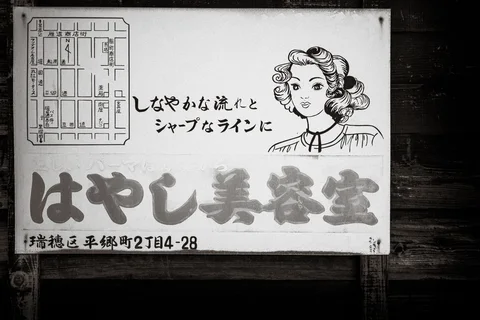 An illustrated woman's face and Japanese lettering fill a weathered rectangular sign in black and white.