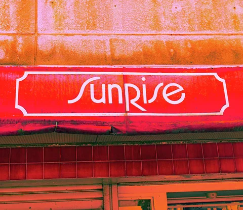 White Sunrise lettering spans a red sign beneath orange-stained exterior wall panels.
