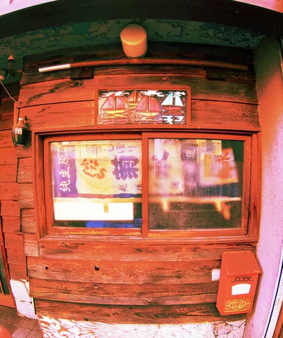 A curved close view shows a red wooden storefront with a small poster-covered window and red mailbox.