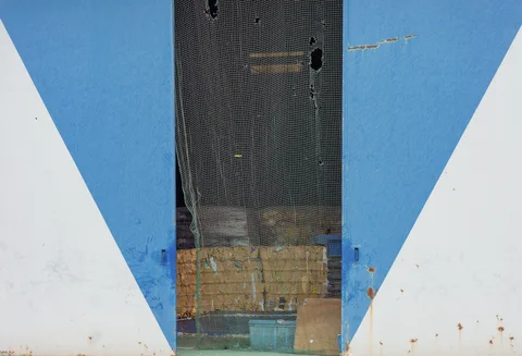 A narrow mesh-covered opening divides large blue and white triangular painted panels with rusty lower edges.