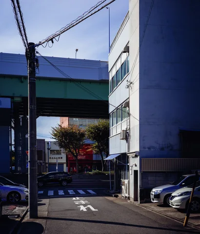 A narrow street passes beneath a green elevated structure between parked cars and pale buildings.