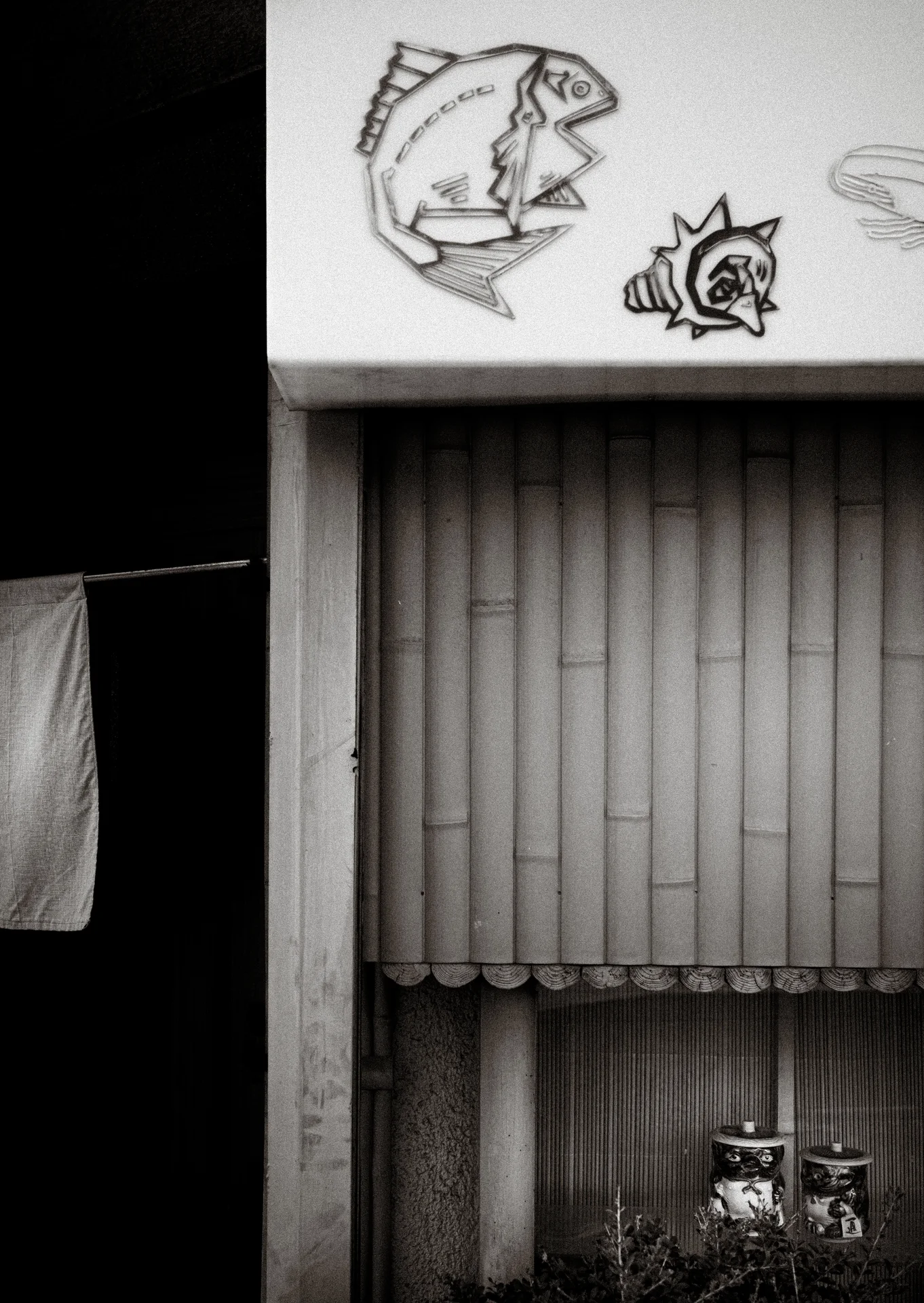 Cartoon fish decorate a pale panel above a tall closed shutter in a black and white view.