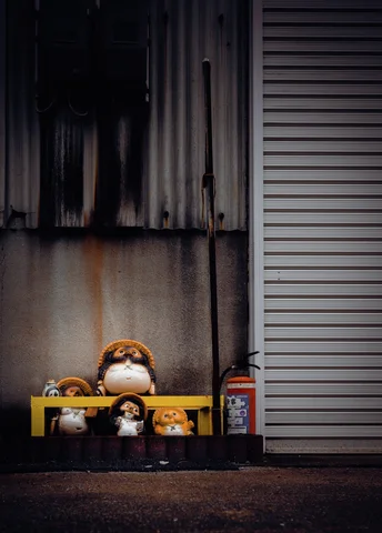 Small rounded animal figurines cluster beneath a yellow bar beside a closed shutter and stained wall.