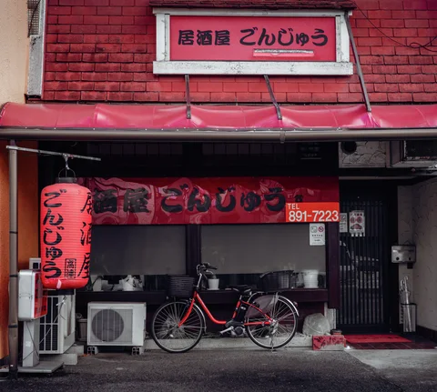 A red bicycle stands outside a brick-fronted restaurant beneath a red lantern and awning.